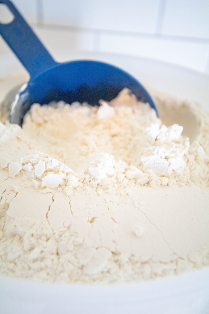 blue measuring cup in clear container of bread flour