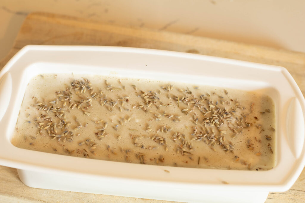 Creamy colored soap in a silicone soap mold topped with dried lavender. 