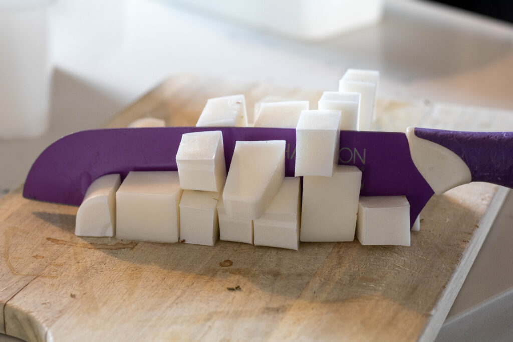 Melt and Pour soap being cut on a wooden cutting board being cut with a purple butcher knife. 