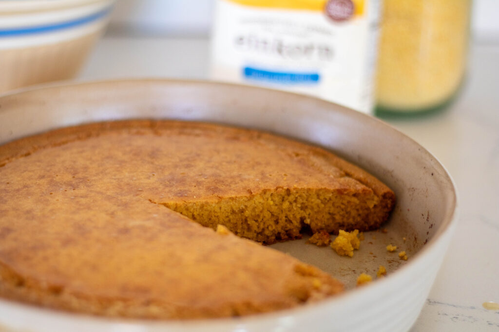 Einkorn cornbread in a round stoneware dish with einkorn flour package out of focus in background