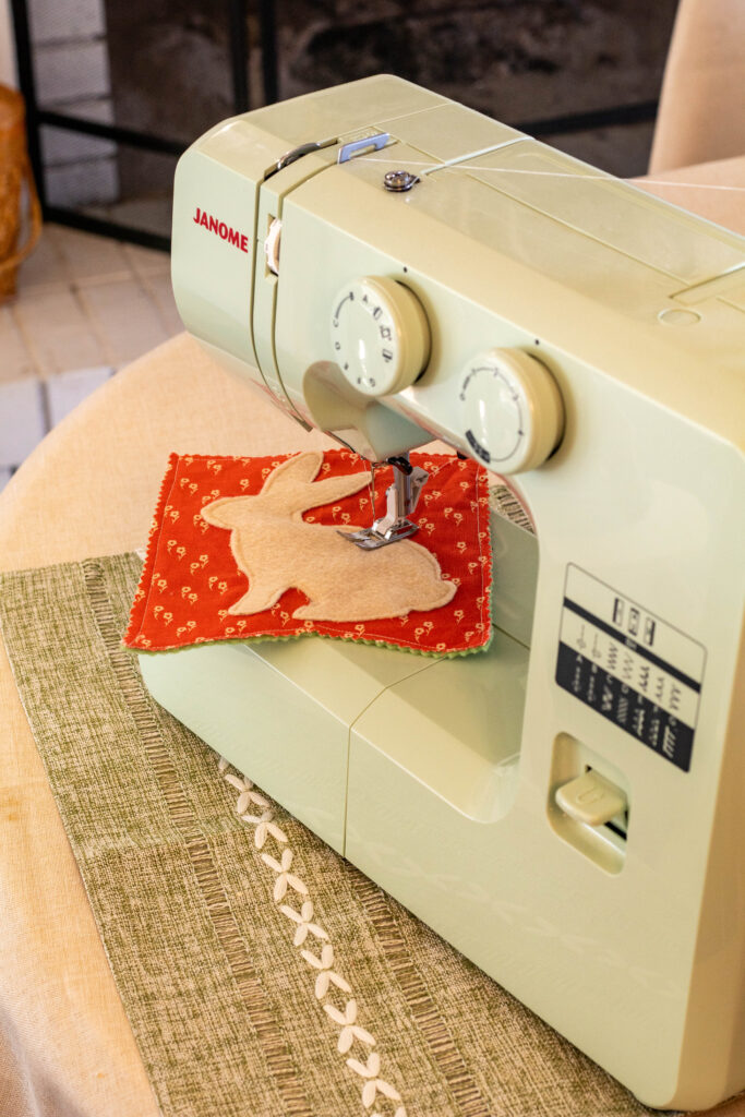 Light green sewing machine with bunny bunting under needle sewing on felt bunny shape.