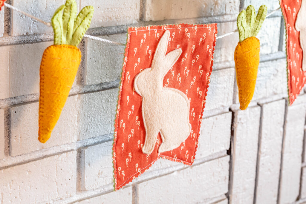 DIY Easter Garldand bunny bunting with felt carrot on either side hanging on what brick fire place.