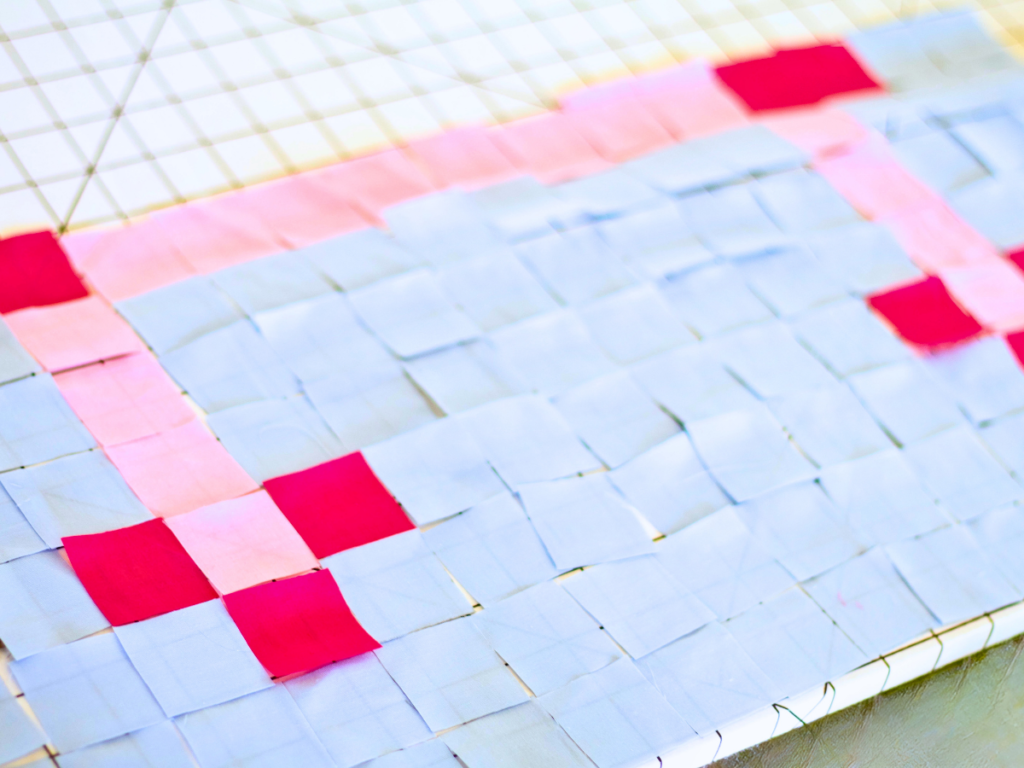 Pixel art quilting fabric squares laid out on a grid.