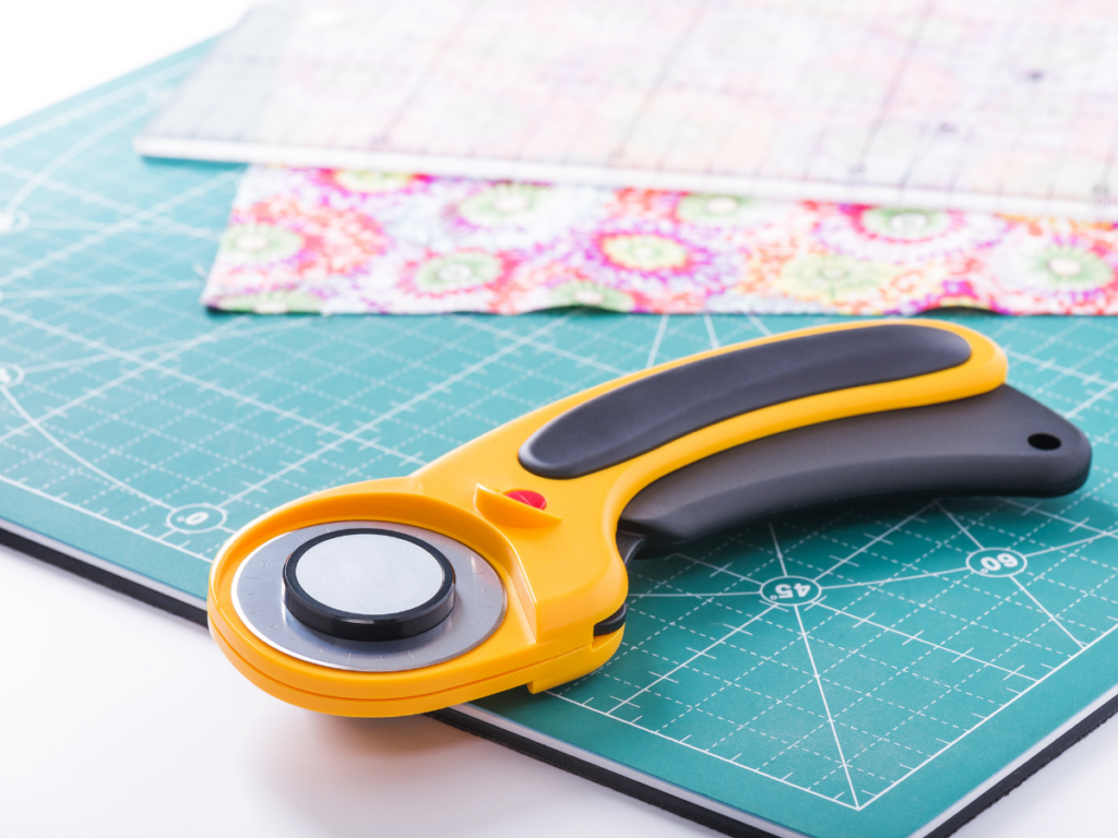 Rotary cutter on a cutting mat with fabric and a plastic ruler in the background. 
