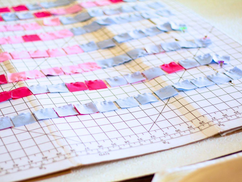 Chains of joined pixel art quilting fabric squares on a ruler grid. 