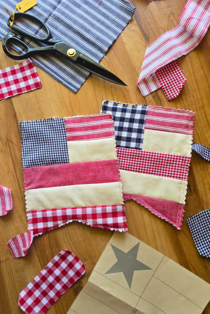 Red white and blue quilted american flag bunting with a wooden background surrounded by fabric pieces, fabric scissors, and a paper template.