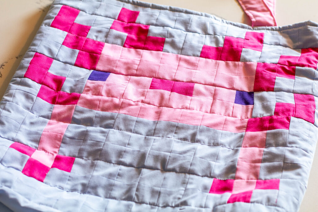 Pixel art quilted tote bag with an axolotl design on it. 